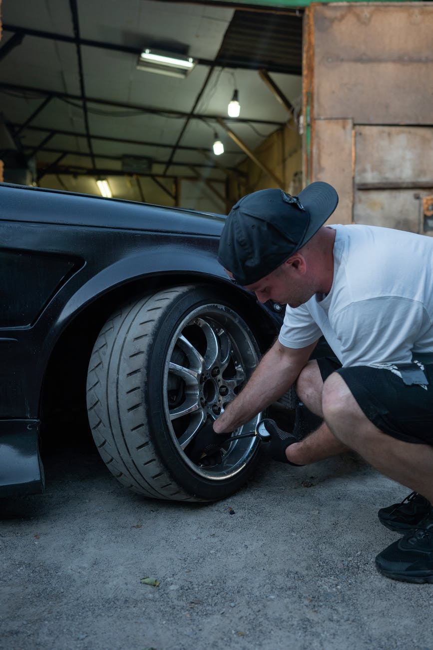 a man wearing a cap checking the tire pressure of a car